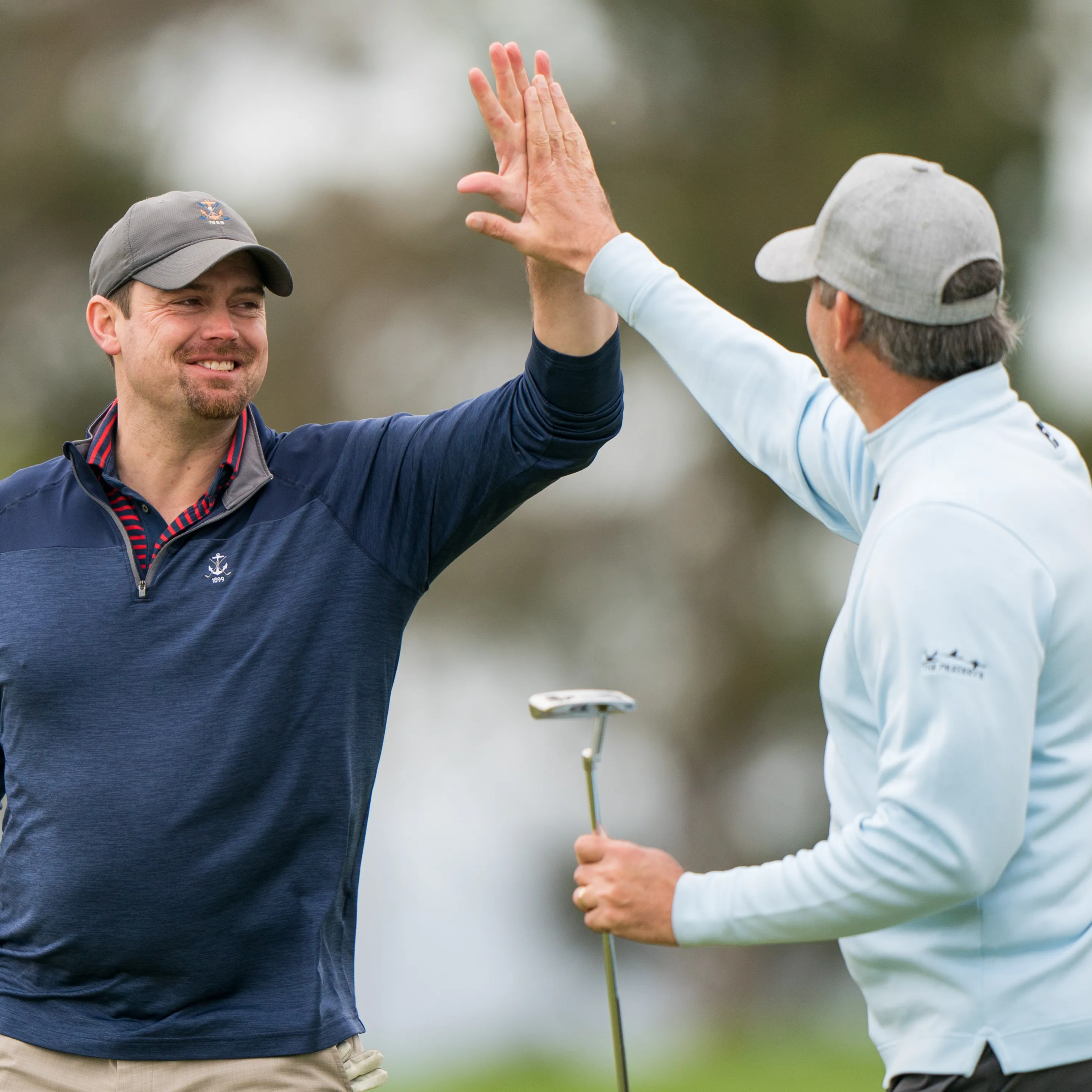 Two golfers high-fiving on the green after finishing a hole at the GCSAA Golf Championships