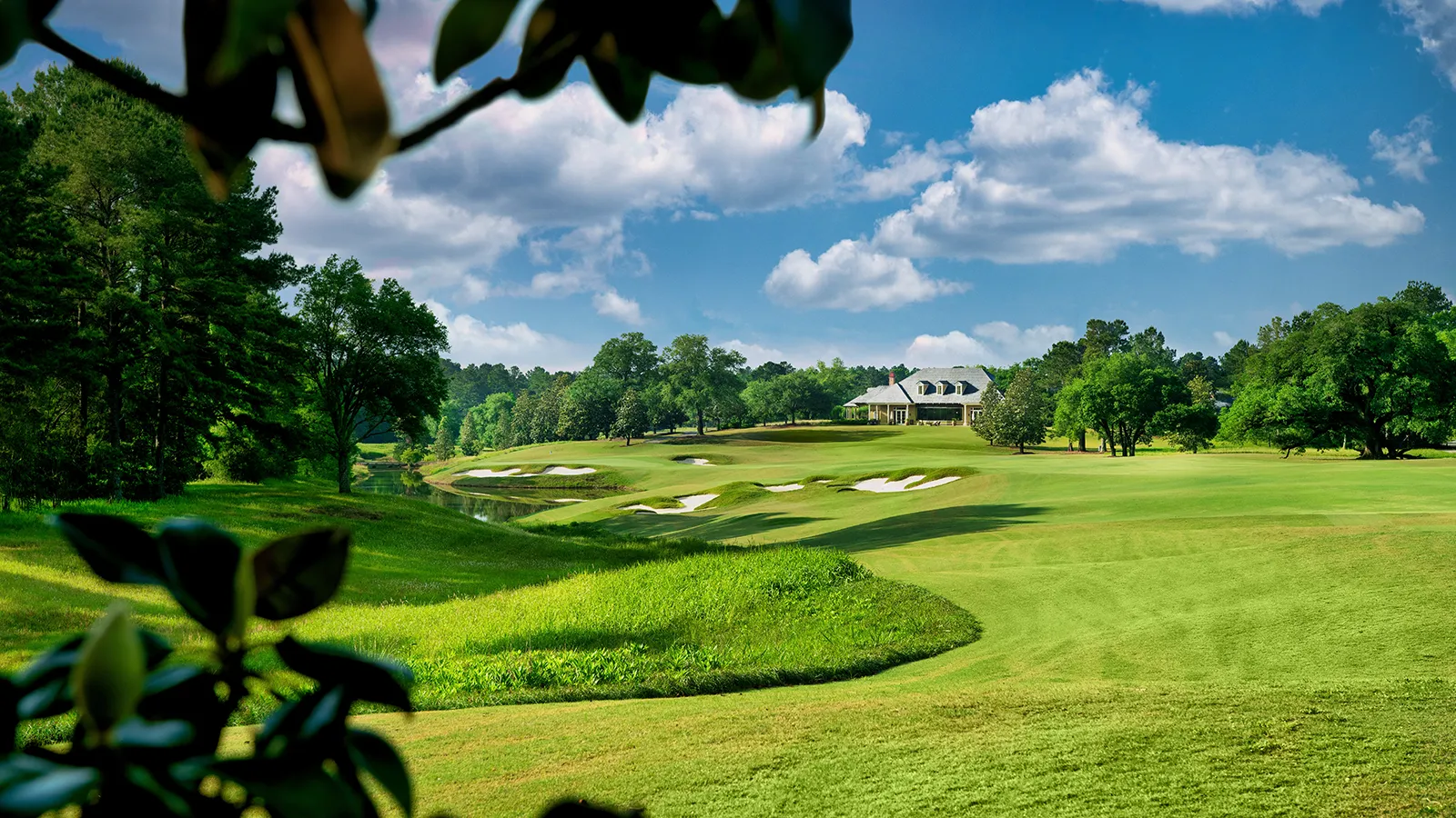 The 18th hole at Fallen Oak Golf Course, with white sand bunkers and a creek leading up to the clubhouse